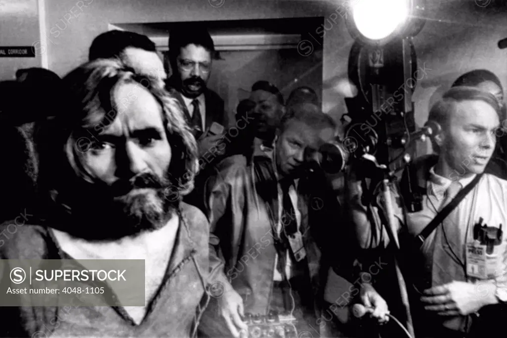 Charles Manson, the 35-year-old cult leader, is escorted through a crowd of newsmen as he arrives at the Los Angeles city jail after a trip from Independence, CA, where he was being held on auto theft charges, December 9, 1969.
