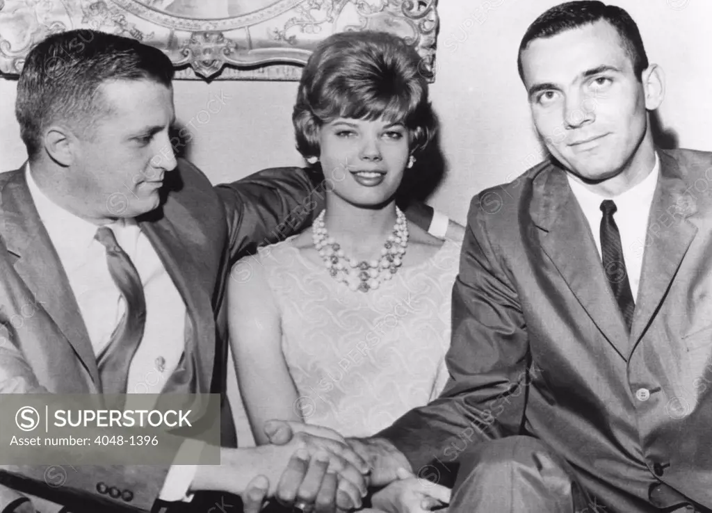 George Steinbrenner (left), shakes hands with Jerry Lucas (right), All-American basketball player. his wife Treva Lucas, Jerry's wife, sits between them. Lucas has just signed a two year contract with the American Basketball League team in Cleveland, Ohio.  May 16, 1962.