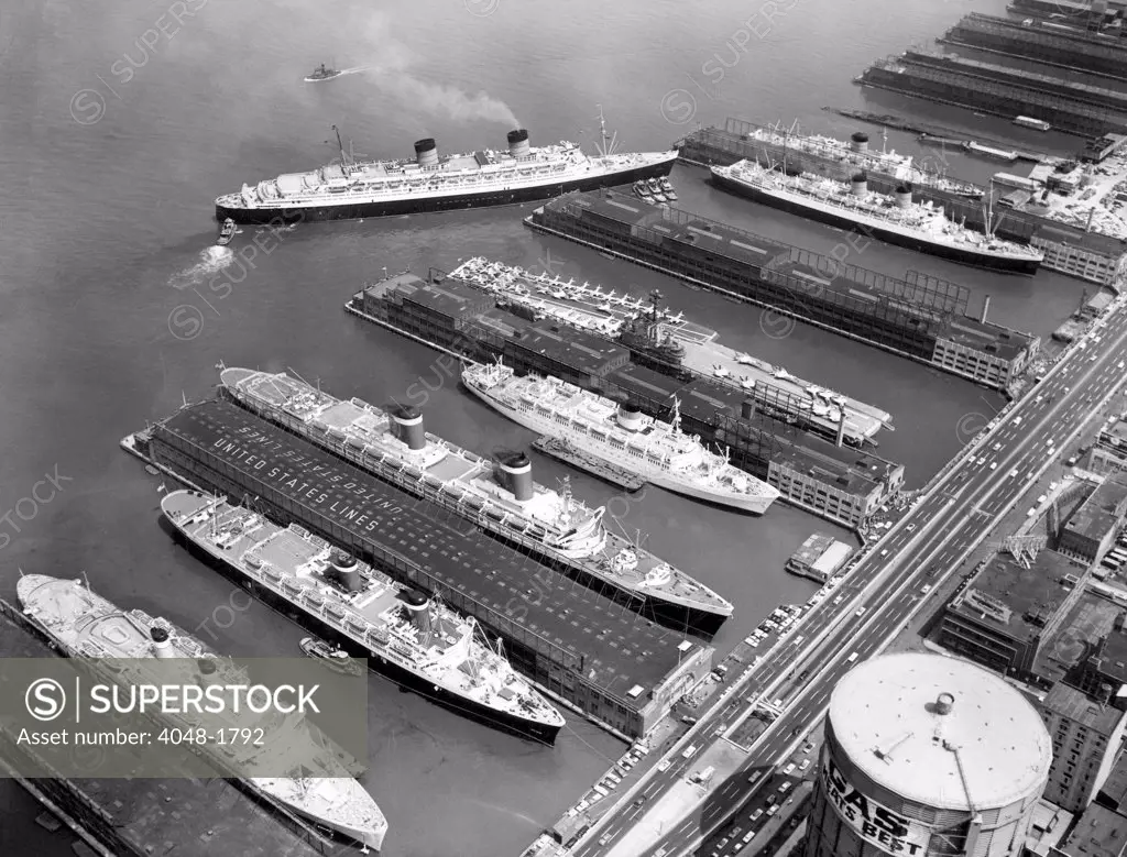 Luxury liners flanking an aircraft carrier at piers along the West Side Highway, from left to right: The Independence, The America, The United States, The Olympia, The U.S.S. Intrepid, The Queen Elizabeth (pulling in), The Mauretania, and The Sylvania, New York City, July, 1961