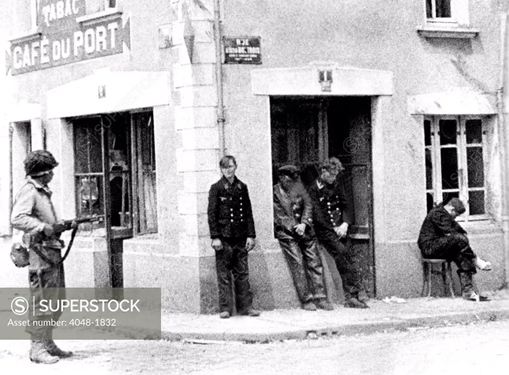 NORMANDY, from Army Signal Corps film, an unidentified American GI stands guard over four Nazis in the streets of Ste. Mere Eglise