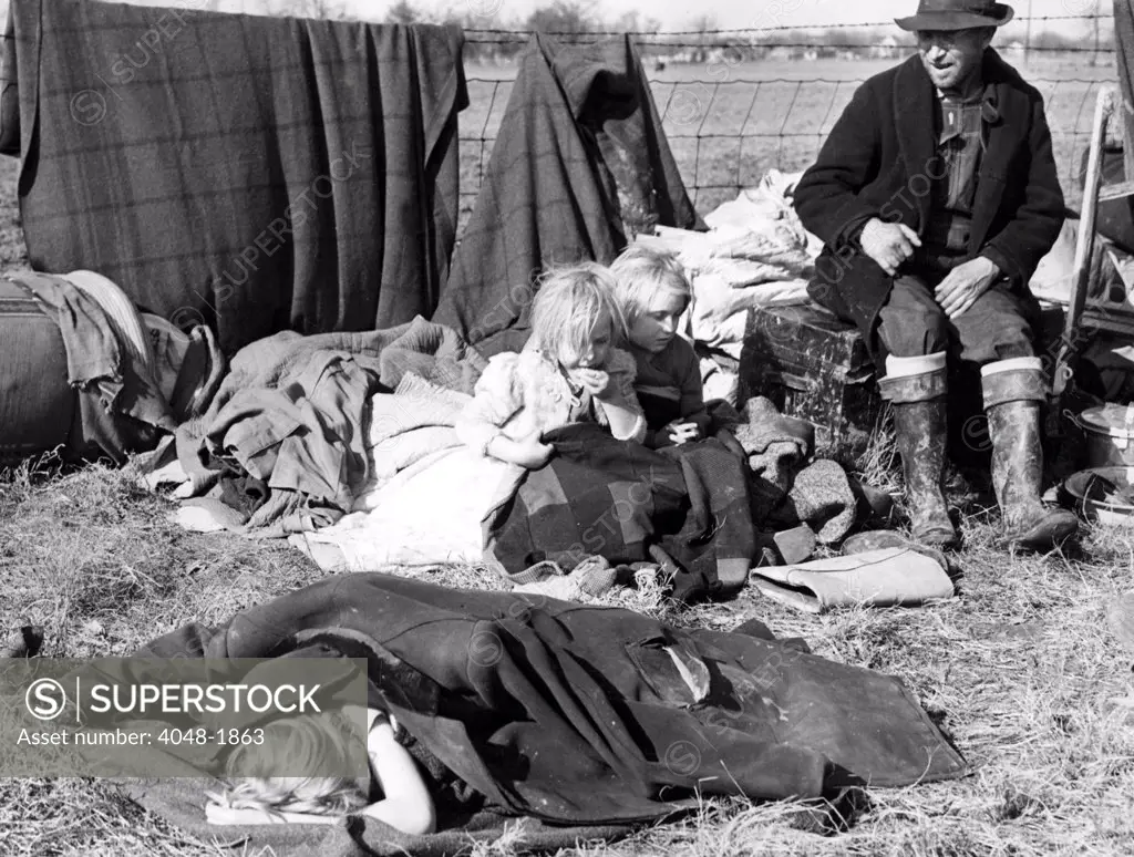 SIKESTON, MO--Evicted from their home, a sharecropper and his three little children sit amonst their meager possessions on the edge of a state highway and wait, along with a thousand other evicted croppers, for aid from the government.  January 11, 1939.