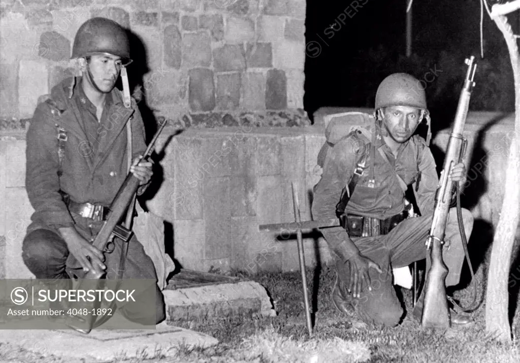Mexico City: Mexican soldiers kneel by cross-marked site where an army trooper was killed by a sniper bullet during fighting with protesting students on October 3, 1968.