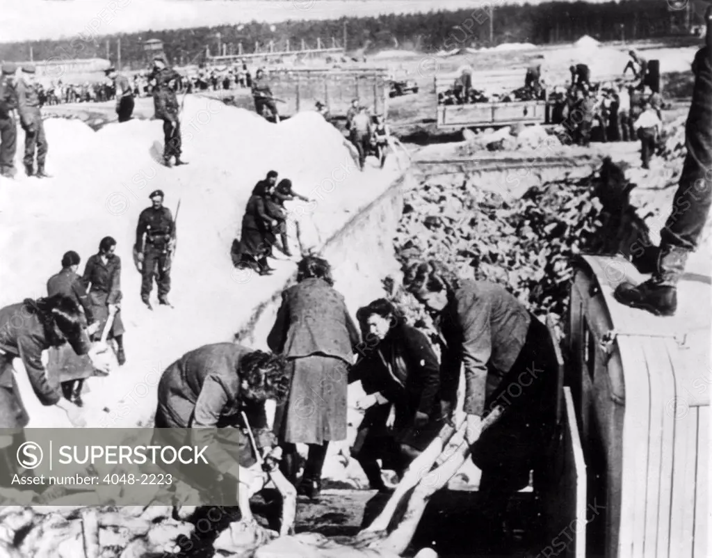4/28/45: At Nazi concentration camp in Belsen, Germany, SS women remove bodies of victims, under British 2nd Army troopers' guard, from trucks before burial in communal grave.