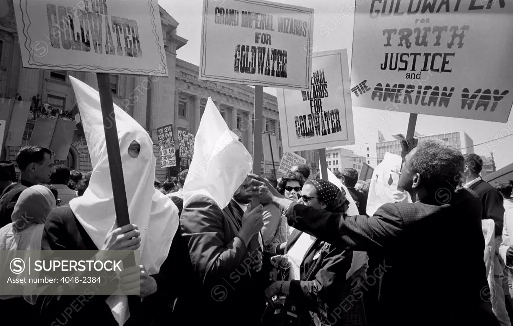 Ku Klux Klan members supporting Barry Goldwater's campaign for the presidential nomination at the Republican National Convention. An African American man pushes back.  by Warren K. Leffler, San Francisco, California, July 12, 1964.