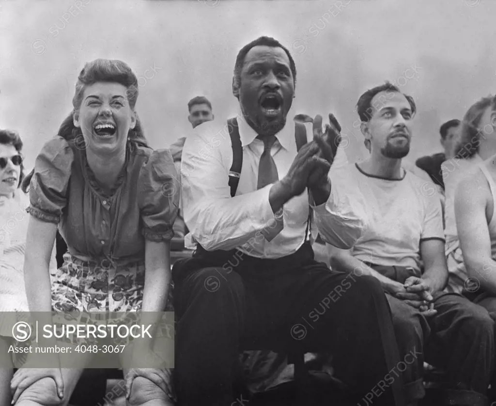 New York City, Paul Robeson (center), Jose Ferrer (right), watching softball with other members of Othello production, Central Park, circa 1943-1944.