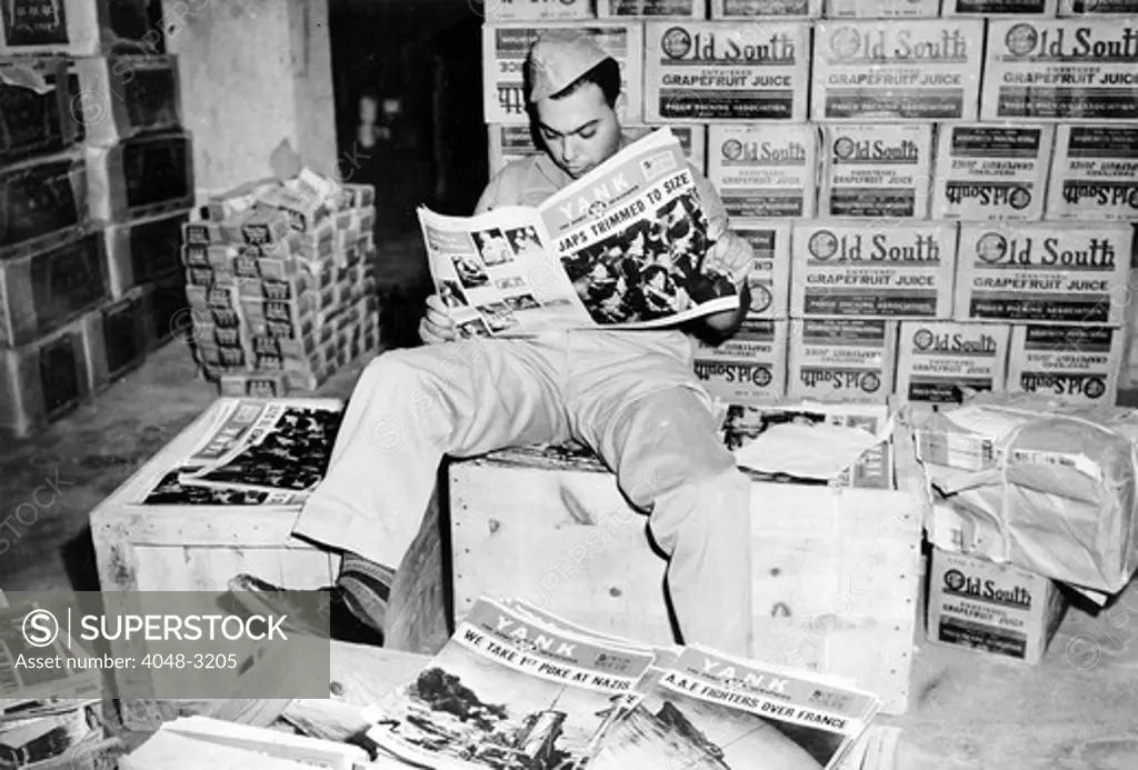 World War II, a U.S. soldier reading Yank, the Army weekly, amid piles of Yank and Old South grapefruit juice. . The headline reads: 'Japs Trimmed To Size', circa 1940-1946.