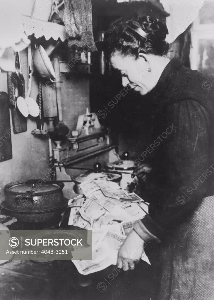 Coffee, original caption: 'Inflation. In Germany after the last war, it was possible to pay 50 million dollars for a nickel cup of coffee, and 35 million dollars for a $35 suit of clothes. This Berlin woman, realizing that fuel costs money, is starting the morning fire with marks 'not worth the paper they are printed on', Germany, circa 1920s.
