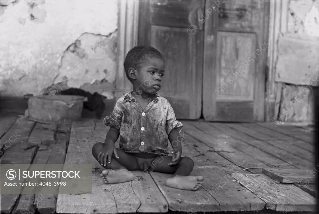 African American child on a dilapidated porch, original title: 'Negro child on porch of dilapidated Trepagnier plantation near Norco', Louisiana, photograph by Lee Russell, September, 1938.