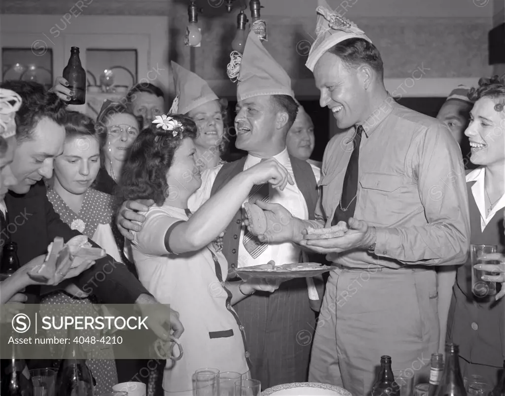 World War II, George Woolslayer (center), soldier and sailor with a party at his home, friends, relatives and fellow workers made up the list of guests, Mrs. Woolslayer (left of center) helps Chief Evans (right), to a sandwich, Pittsburgh, Pennsylvania, photograph by Alfred T. Palmer, August, 1942