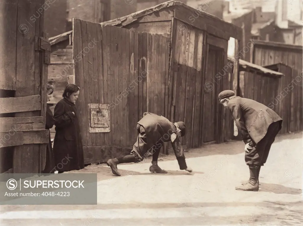 Boys playing a dice game, from original caption: 'Red St. Clair and chum shooting craps in front of Murphy's Branch at 11:00 A.M. Thursday, a school day. Red is boss of the gang here. The girls hang around and watch the boys, skip rope with them' St. Louis, Missouri, photograph by Lewis Wickes Hine, May 5, 1910