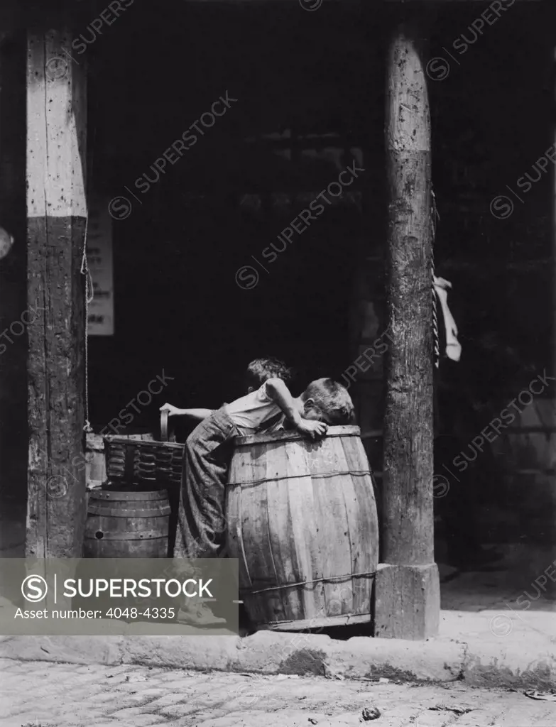 Small boys picking from barrels, from original caption: 'This boy and brother were picking discarded fruit out of barrels in market near 14th St. N.Y. City. He was also (when apparently unobserved) stealing good fruit from their barrels', New York City, photograph by Lewis Wickes Hine, July, 1910
