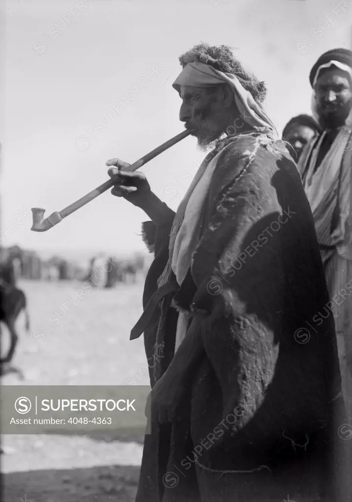Bedouin man smoking a long pipe., photograph 1920.