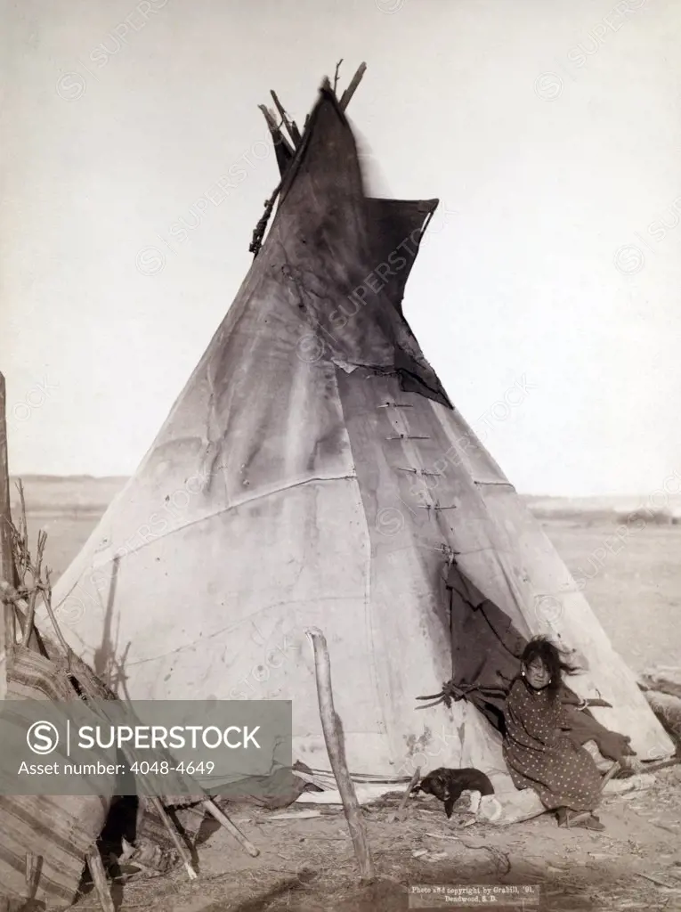 A young Oglala girl sitting in front of a tipi, with a puppy beside her, probably on or near Pine Ridge Reservation. Pine Ridge, South Dakota.  Photo by John C. Grabill. 1891