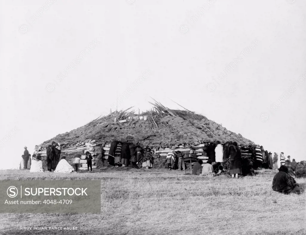 Sioux Indian dance house, log building with sod roof and American Indians outside, photograph, 1911