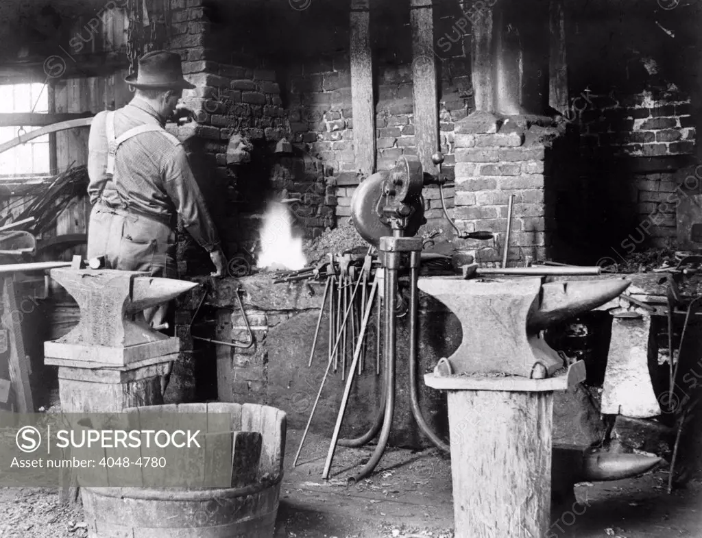 Occupational portrait of a blacksmith, in his smithy with anvils, ca. 1906