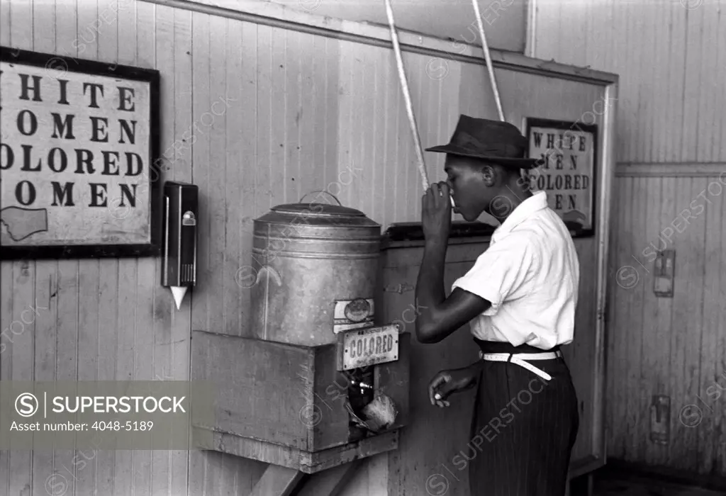 Original caption reads: 'Negro drinking at colored water cooler in streetcar terminal', by Lee Russell, Oklahoma City, Oklahoma, July, 1939.