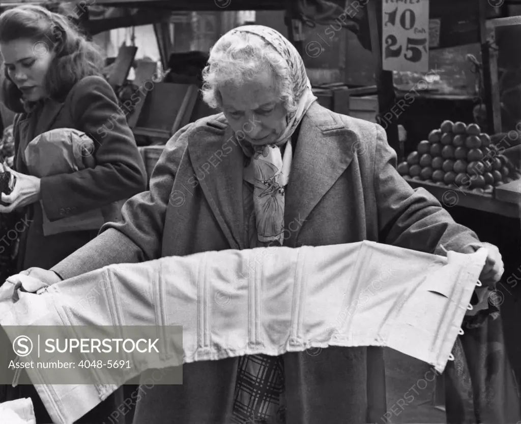Elderly woman evaluating a corset at a pushcart market on Belmont Avenue, Brooklyn, New York. 1958.