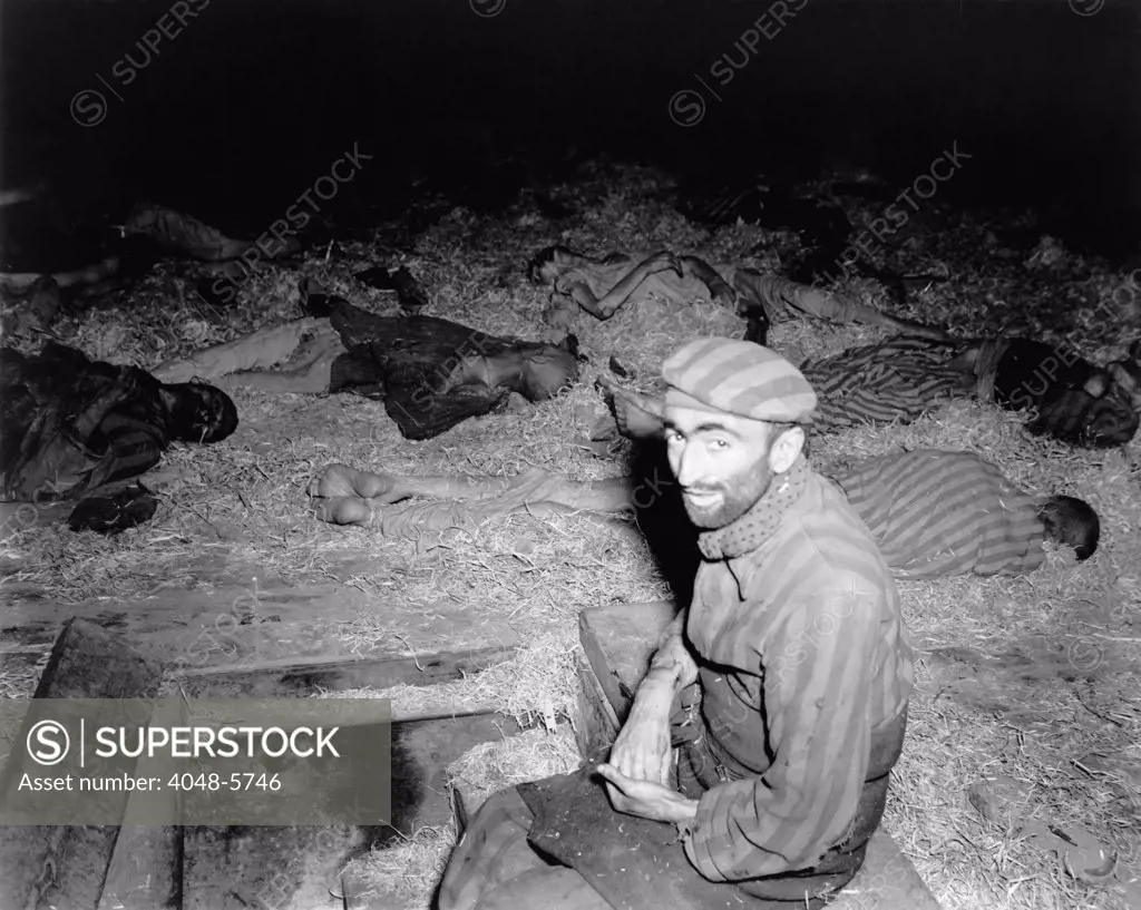 Emaciated Frenchman sitting among the dead in prison camp, Nordhausen, Germany after liberation by First U.S. Army on April 11, 1945.