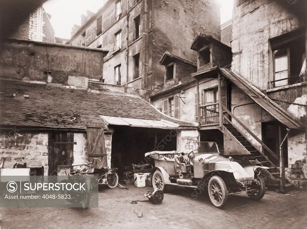 Automobile and two motorcycles in courtyard on Rue de Valence, Paris, photographed by Eugene Atget with a large-format wooden bellows camera. Ca. 1920.