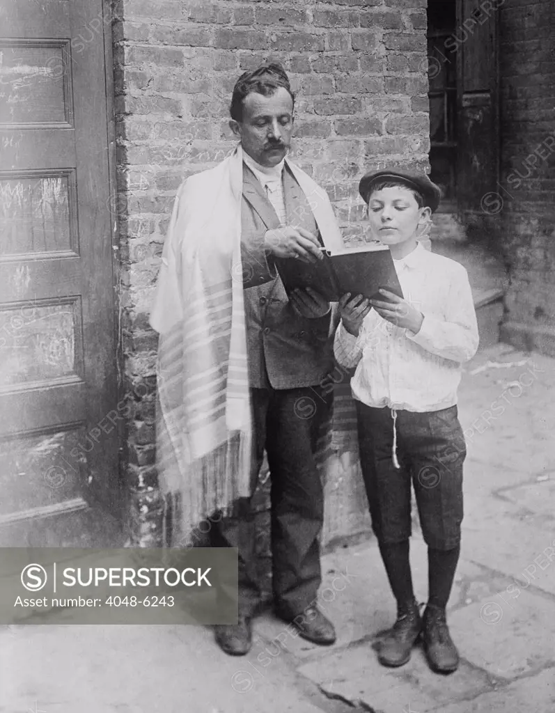 Jewish man wearing a prayer shawl and boy reading from Hebrew Bible on Yom Kippur, in New York City. Ca.1910.