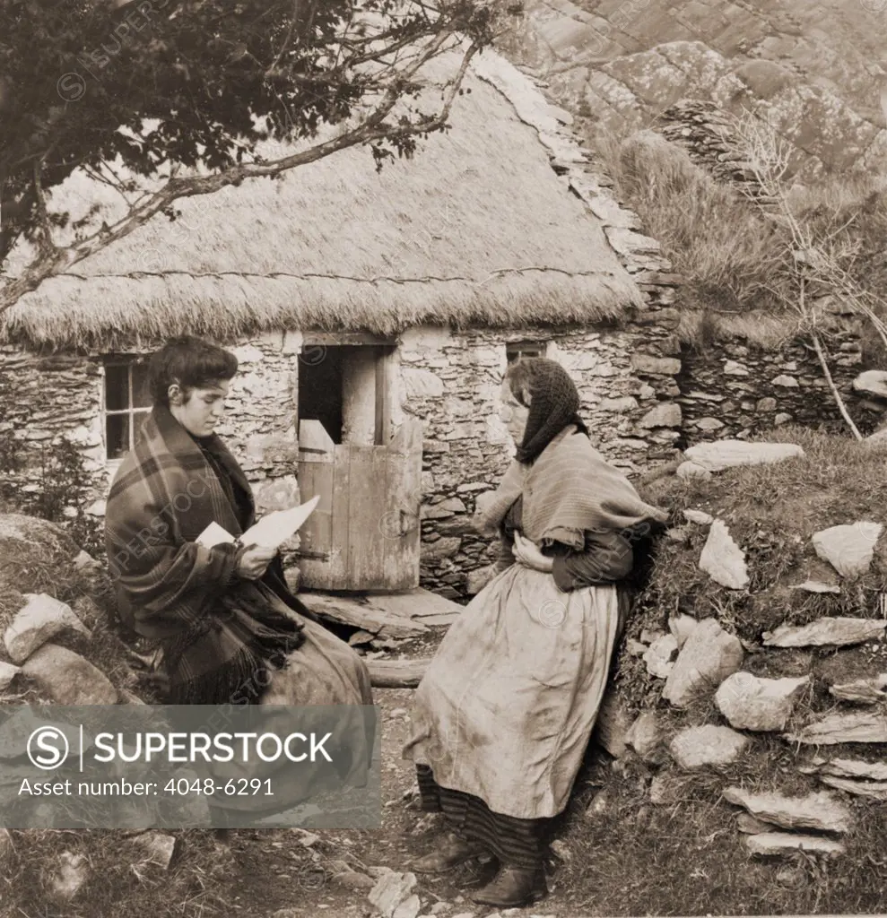 A LETTER FROM PAT IN AMERICA. Young Irish woman reading a letter from a relative  in America to an older woman outside of a thatch-roofed stone cottage.