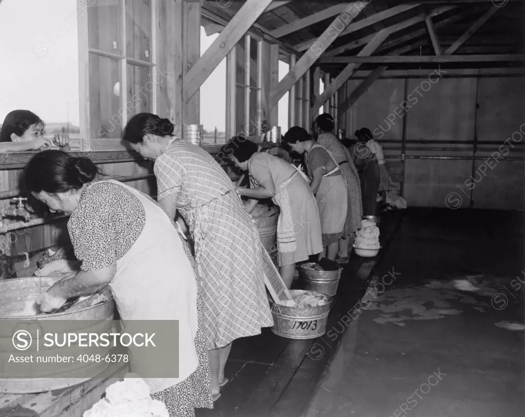 Japanese American women, laundering their families' clothes in metal washtubs during their three month incarceration at Pinedale Assembly Center. 4,823 internees were later sent to permanent internment camps for the duration of World War II. Ca. April 1942.