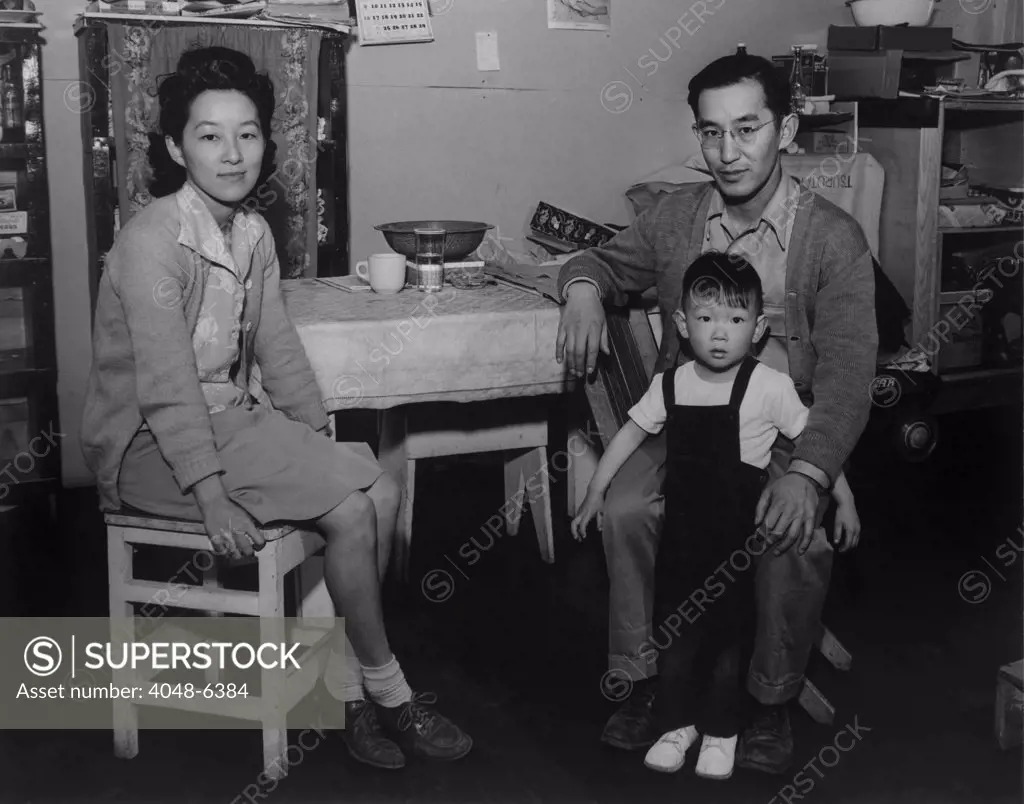 Japanese American family interned at Manzanar Relocation Center during World War II. Mr. and Mrs. Henry J. Tsurutani pose in their barracks with their son, Bruce. 1943 photograph by Ansel Adams.