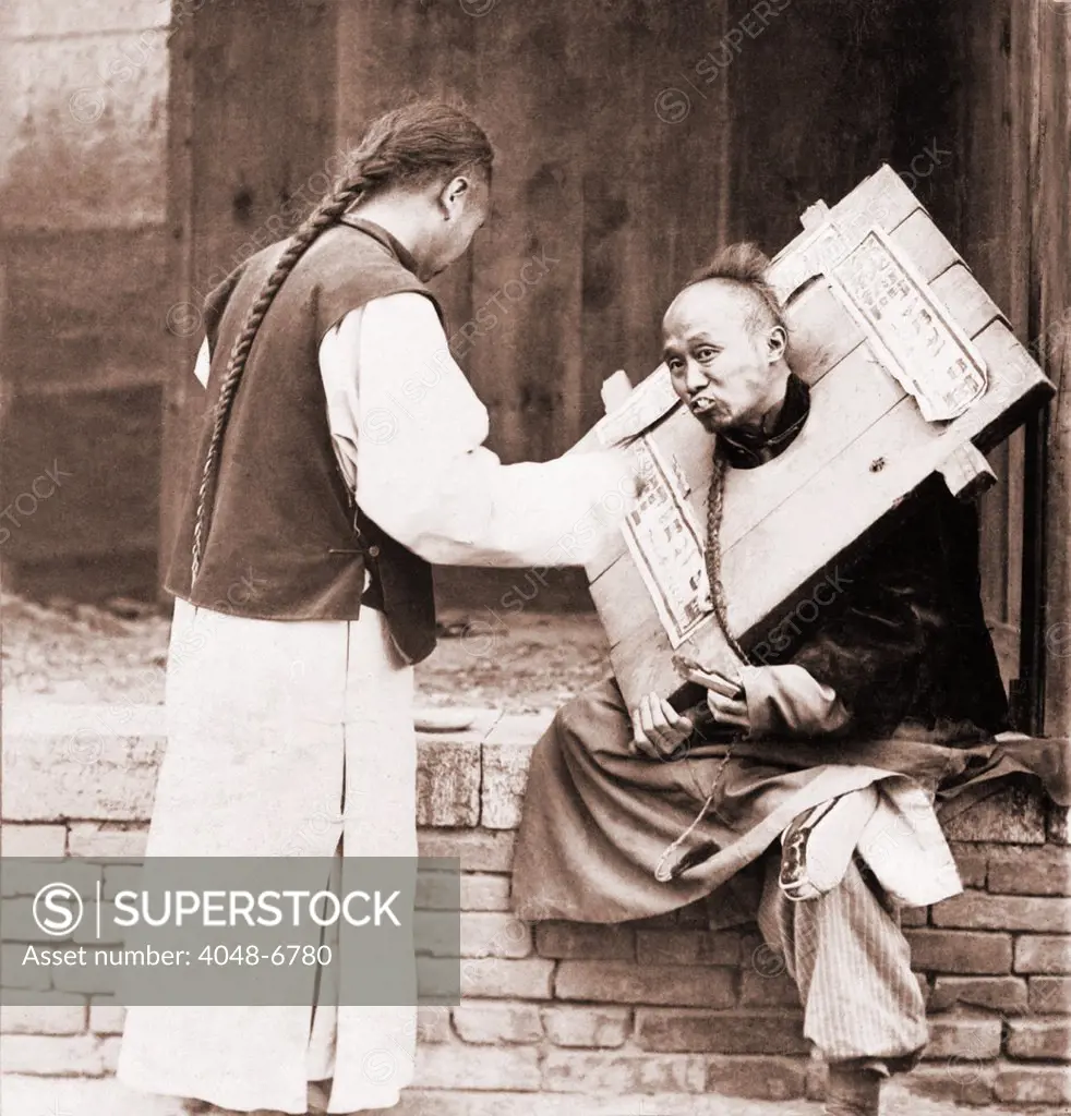 Charitable Chinese man feeding a criminal in a cangue. Petty criminals were sentenced to wear the canque, often for a couple of months, and display themselves in public places. At best they were humbled by dependence on others to be fed, at worst, they might starve to death. The sign on the cangue describes the man's crime. Ca. 1905.