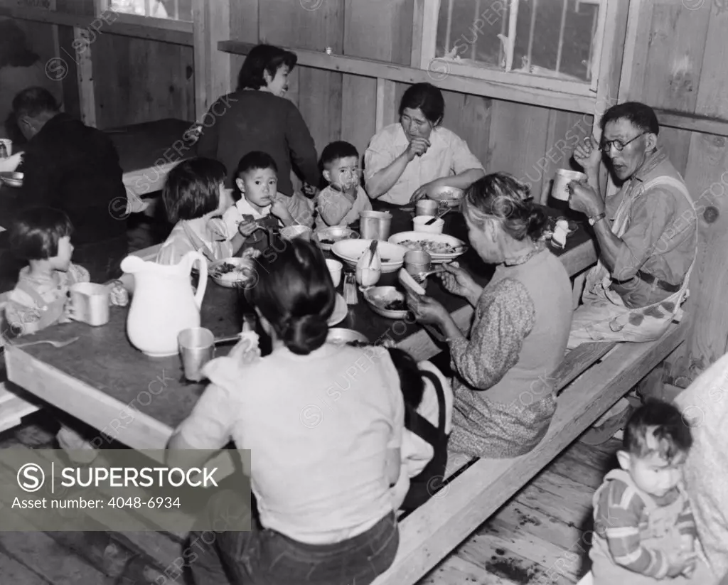 Multiple generations of Japanese Americans at meal time in the Manzanar Internment Camp barracks dining area.