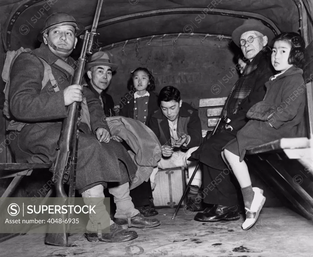 Under armed guard, parentless children and a pastor sit in the back of truck for their evacuation from Bainbridge Island, during the World War II internment of Japanese Americans. The orphans were interned at Manzanar's 'Children's Village,' the only orphanage in  internment camps, to which 100 children from Alaska to San Diego were sent for the duration of the war. 1942.