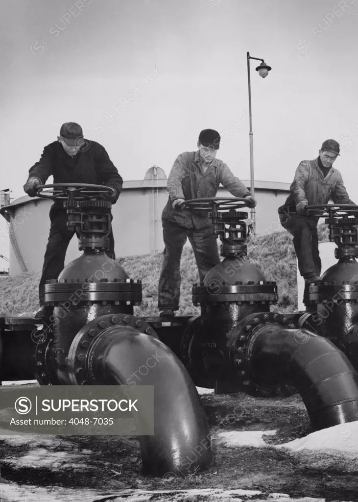 Men turn the wheels of large valves that regulate the flow of oil into oil tankers at a U.S. Atlantic coast seaport. Ca. 1944.