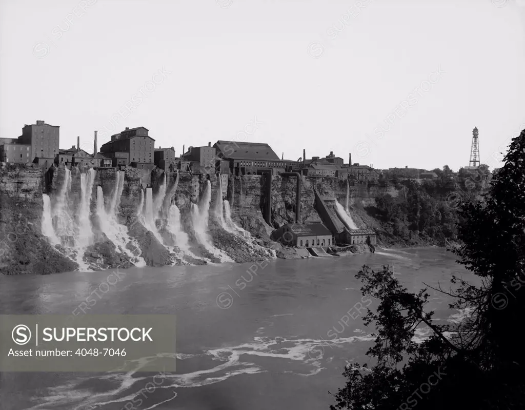 A cluster of factories built on and into the walls of the Niagara River Gorge. Water diverted from above the great Niagara Falls flows from the factories power generation plants. Ca. 1895.