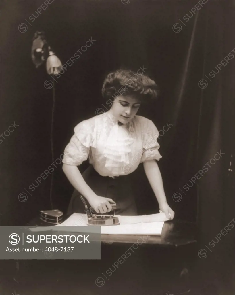 General Electric advertising photo of a woman using an electric iron plugged into light socket, ca. 1908.