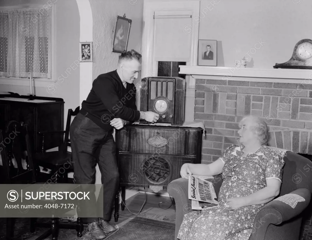 A husband tunes the radio while his wife holds populist right-wing radio priest, Father Coughlin's newspaper SOCIAL JUSTICE, with a headline, STALIN ORDERS WORLD REVOLUTION. This comfortable middle class home was in Royal Oak, Michigan, where Father Coughlin was a priest. 1938.