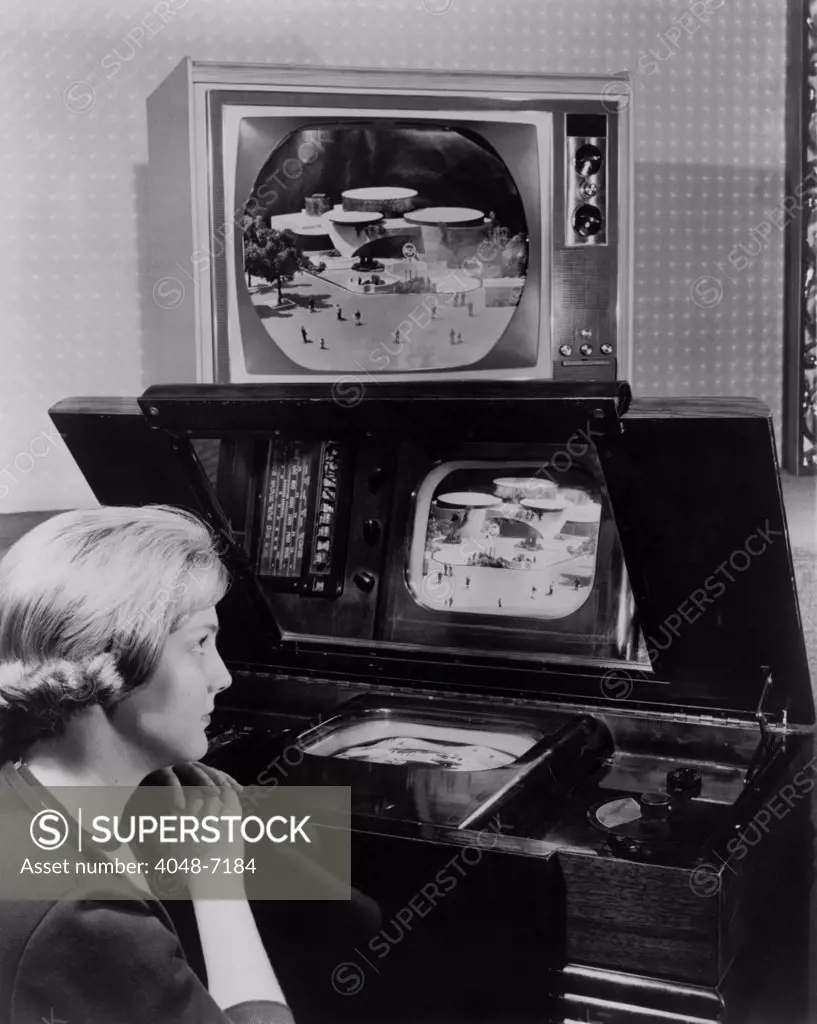 Woman looking at two television sets. One, similar to a set demonstrated at the 1939 New York World's fair, has a small screen incased horizontally in a large wooden cabinet and is viewed from a reflective mirror. The other, now displayed 25 years later at the 1964 New York World's fair, is a large screened color television.