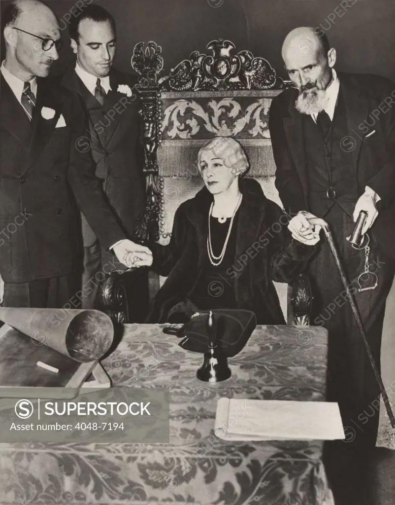 Mrs. Bess Houdini, widow of the great magician, sitting in a chair with her business manager, Edward Saint (to her left holding handcuffs), and others, during a seance, in an effort to contact the spirit of Harry Houdini. 1936.