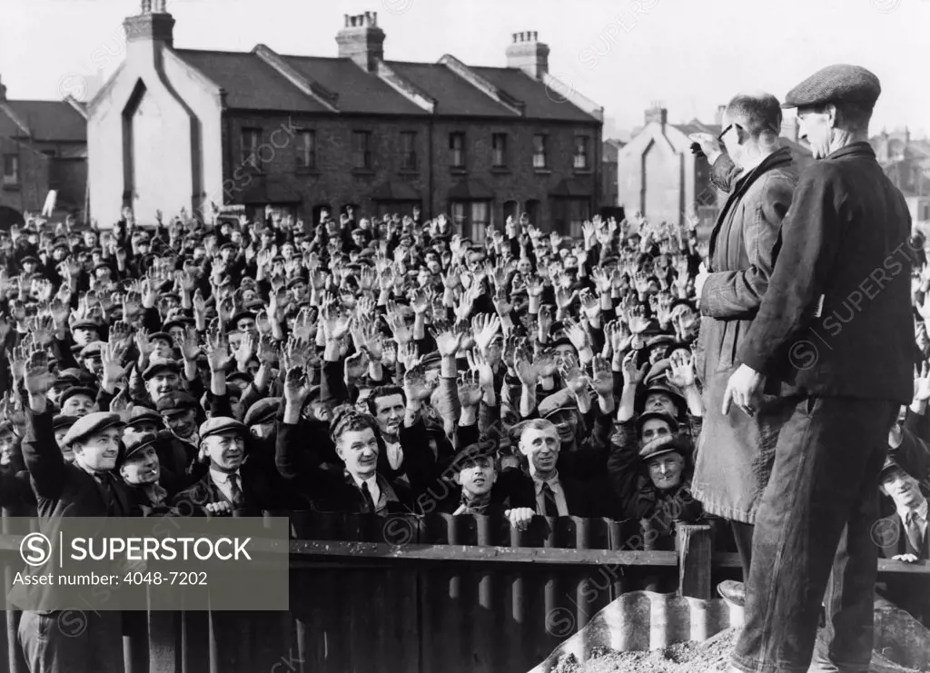 Strikers at the Royal Albert Docks, London, raising their hands in a vote of confidence for strike leader Thomas Powell, seen in right foreground, wearing glasses. 1945.