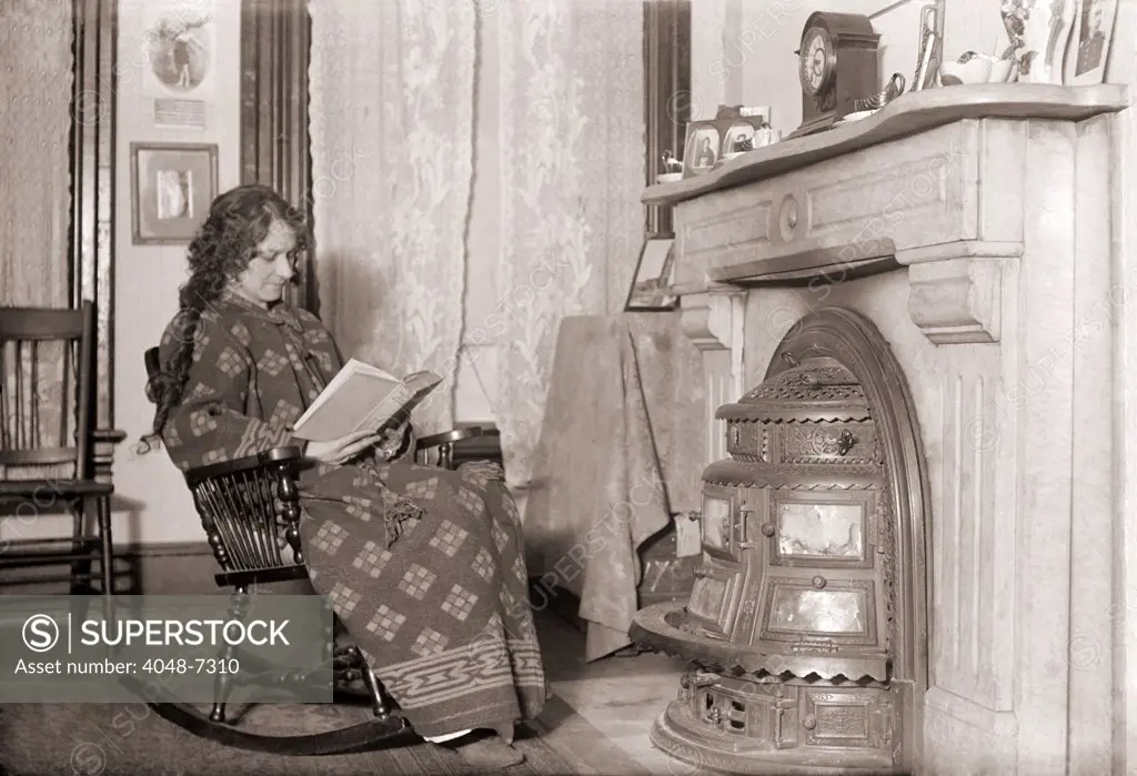 In a heavy robe, a woman reads in front of a coal stove installed in her fireplace.