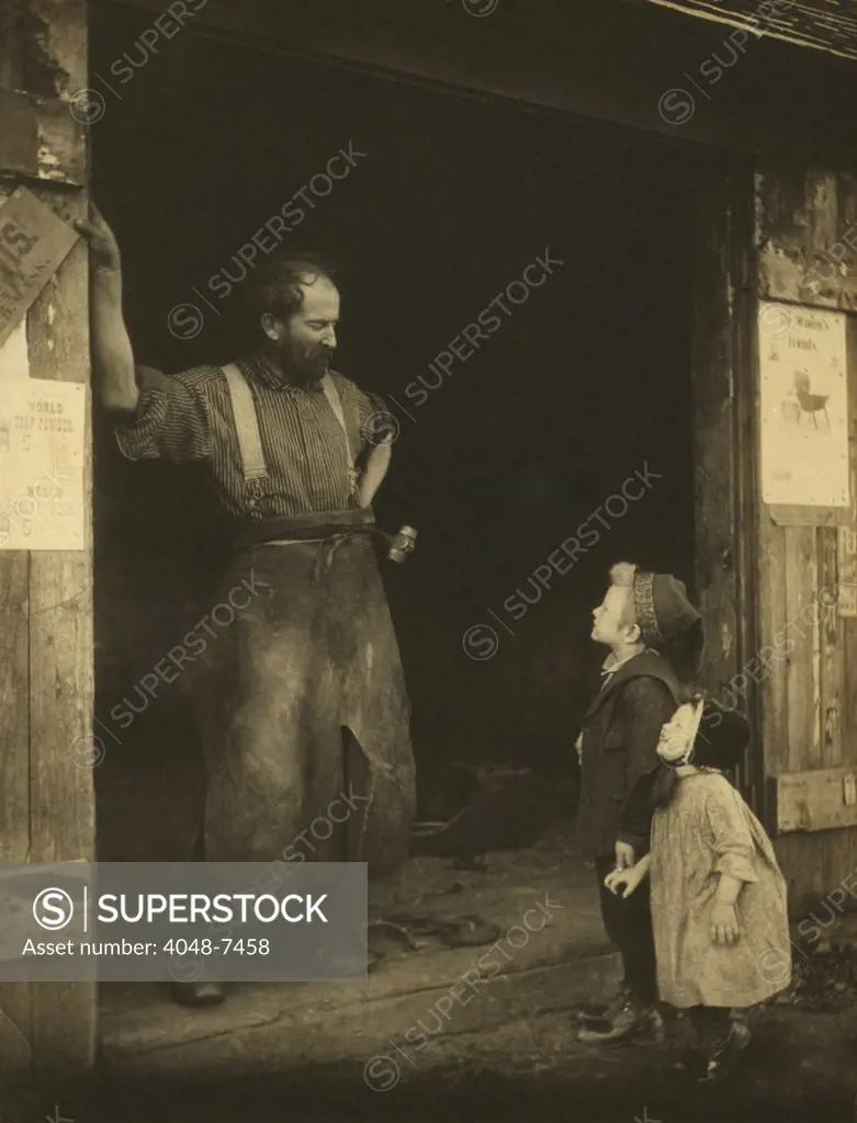 An leather aproned blacksmith in the doorway of his forge talking to two youngsters. Photograph by Frances Stebbins Allen, c. 1900.