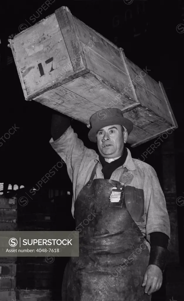 Porter at Paris' Central Market wearing a special, narrow-brimmed, hard-crowned hat to help balance the crate of fish he is carrying on his head. 1946.