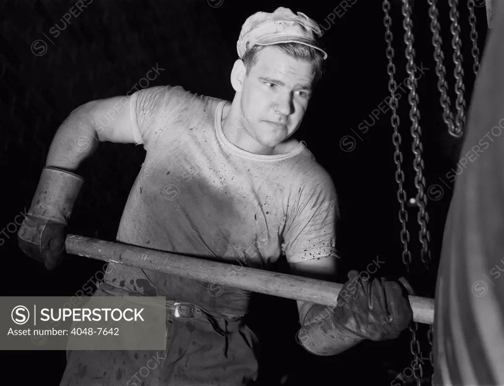 Defense worker at the Goodrich rubber plant molding rubber with a wooden paddle. December 1941.