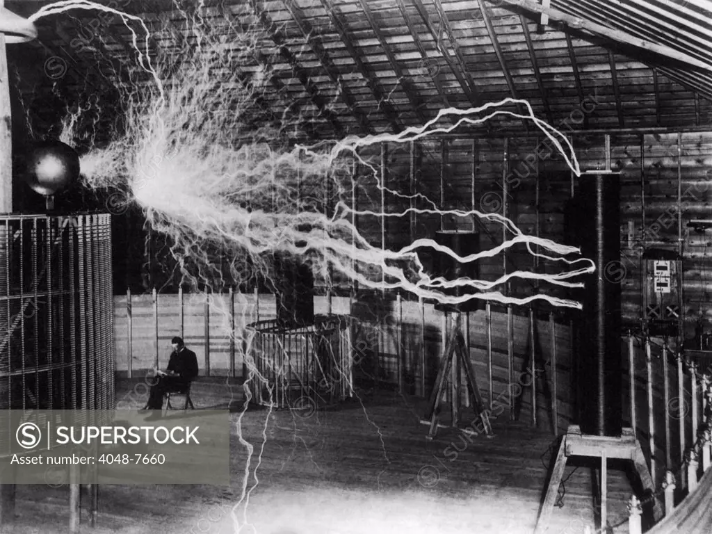 Nikola Tesla 1856-1943 created a double exposure photograph of himself reading undisturbed by a 22 foot long discharge of artificial lightning of millions of volts of electricity.