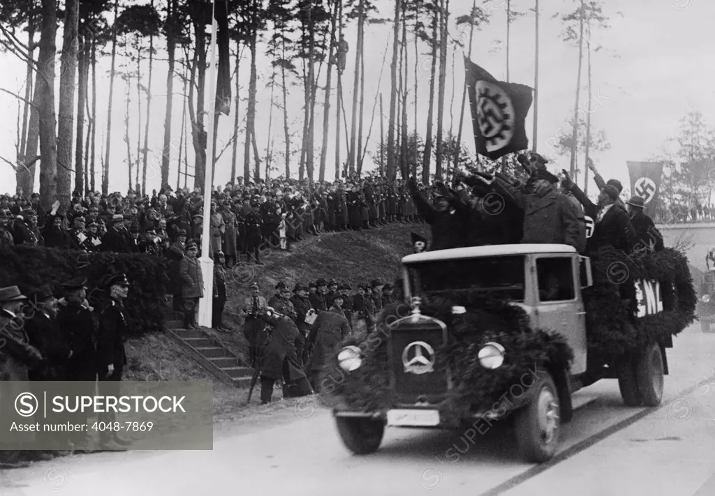 Hermann Goring in group at left receives the Nazi salute from men riding in a decorated Mercedes truck during inaugural ceremonies for the German Autobahn. April 4 1936. LC-USZ62-128817
