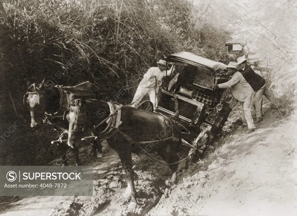 Three men in suits push a horse-drawn carriage stuck in the mud on a Puerto Rican road in 1912