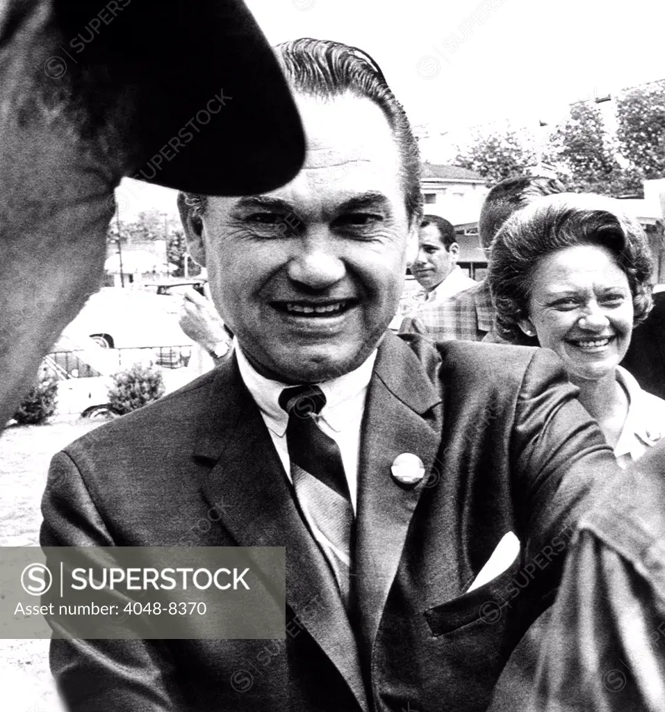 Lurleen Wallace a surrogate candidate for her husband, stays in the background as her husband, Governor George Wallace, shakes hands with voters in Clayton, Alabama. May 3, 1966.