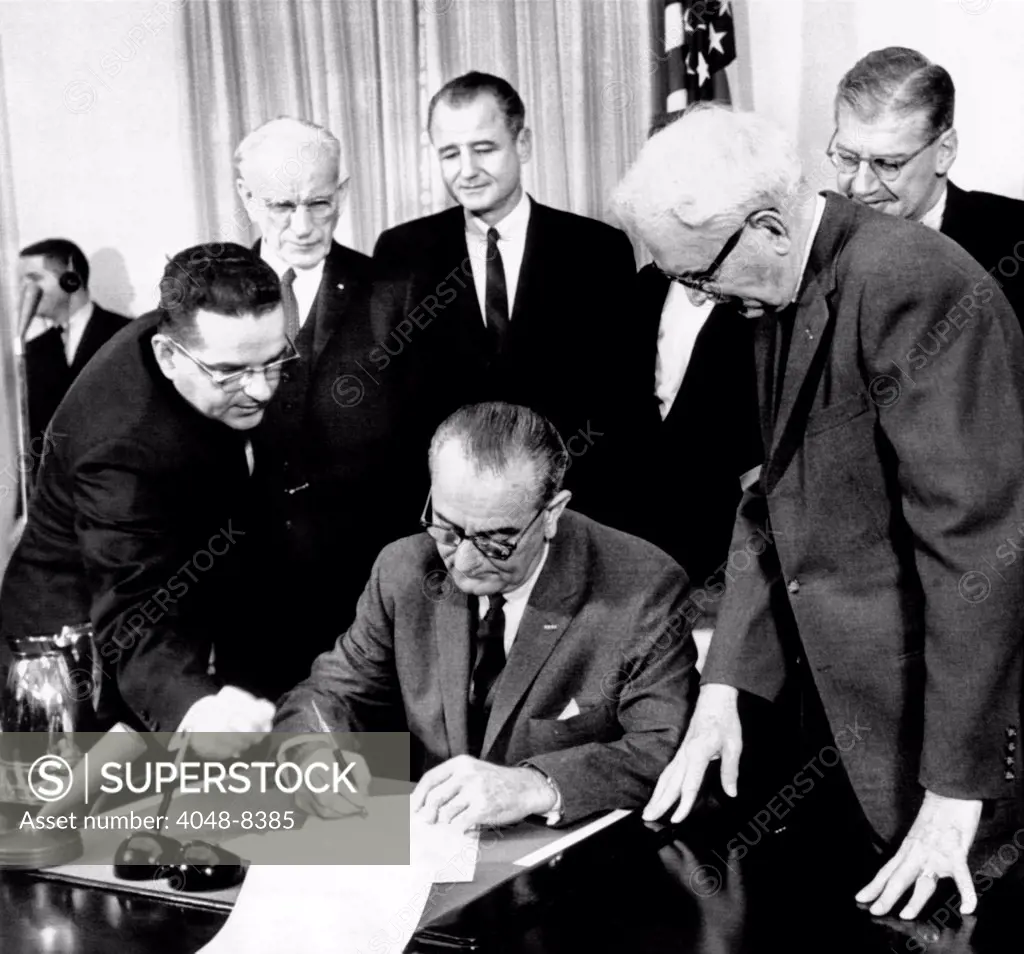 President Lyndon Johnson signs the 24th Amendment to the Constitution. It prohibits payment of a poll tax or other types of tax as a requirement for voting in federal elections. Standing, L-R: Bernarde Boutin, John McCormack, George Smathers, Andrew Biemiller, Spessard Holland, Joseph Rauh. Feb. 4, 1964.