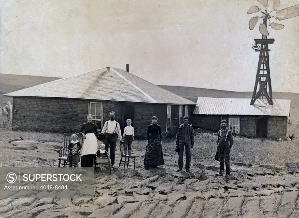 A farm family standing in front of sod house and windmill. Coburg, Nebraska 1885