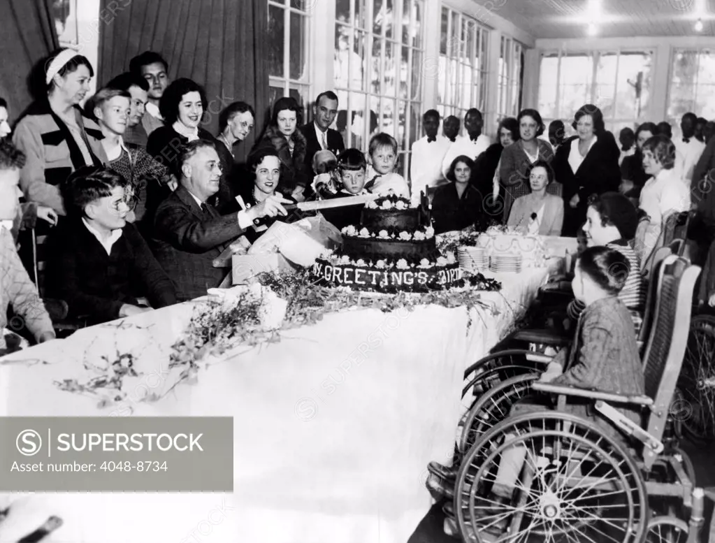 President-elect Franklin Roosevelt celebrating his 51st birthday. FDR cuts his birthday cake at the sanitarium for polio victims at Warm Springs, Georgia. Eleanor stands behind him on left. Jan. 30, 1933.