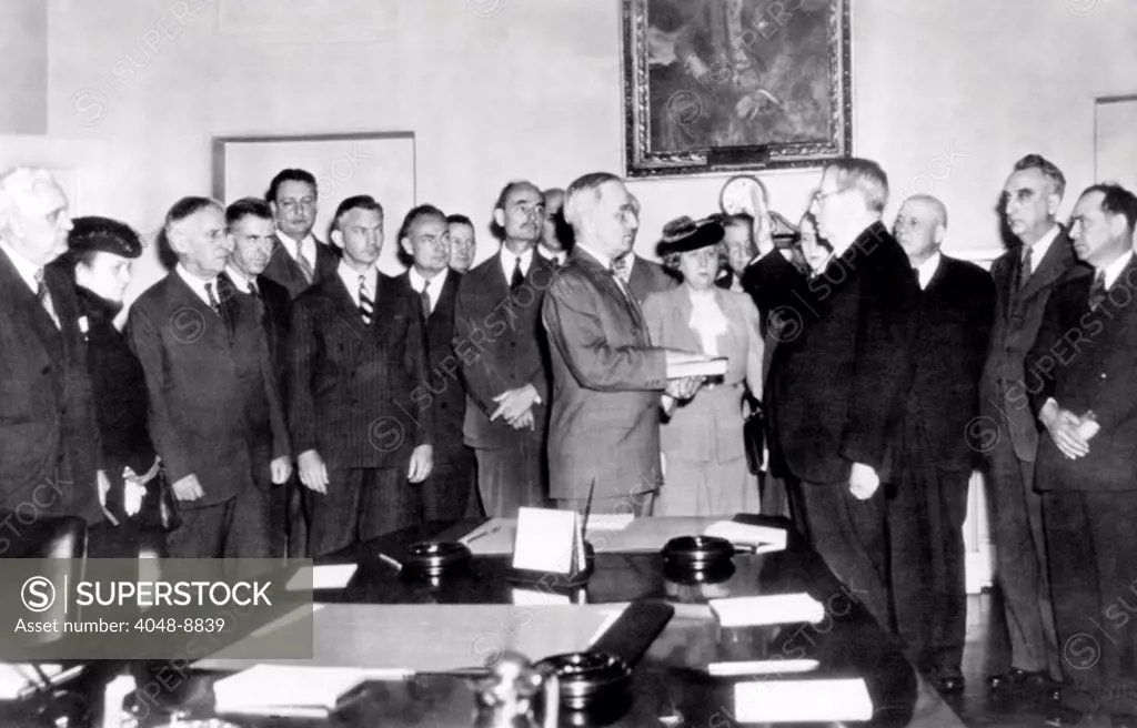 Vice President Harry Truman took the oath of office in White House Cabinet Room after Franklin Roosevelt's death. L-R: First man unidentified, Perkins, Stimson, Wallace, Krug, Forrestal, Wickard, Biddle, Truman, Mrs. Truman, Ickes (just behind Mrs. Truman), Margaret Truman, Chief Justice Stone, Sam Rayburn, Vinson, Joe Martin. April 12, 1945.