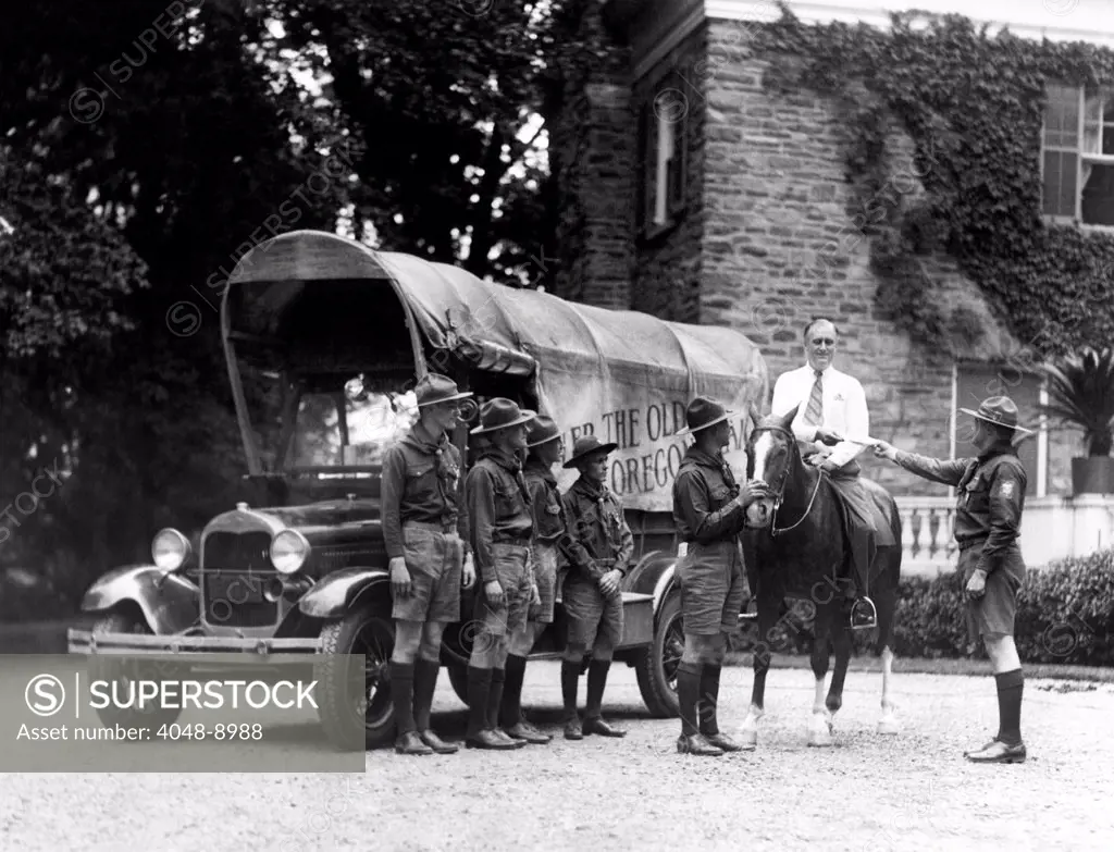 Governor Franklin Roosevelt on horseback with five Boy Scouts' on the start of their cross country trip. The scouts have rigged the antique wagon of pioneer writer Ezra Meeker to a truck, for the drive to the covered wagon centennial to be held at Independence Rock, Wyoming. July 25, 1930.